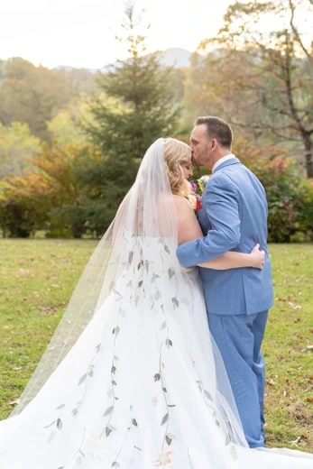 Groom kissing the bride's forehead in a sunlit field