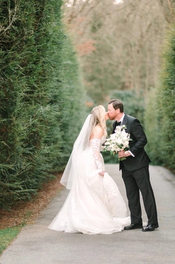 Bride and groom kissing on a path lined with tall hedges